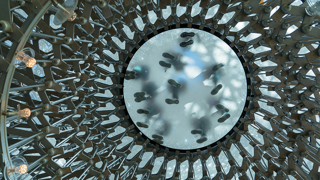Photo: Looking up at people stood on a glass floor of The Hive modern art installation at Kew Gardens; Source: Photo by Nick Fewings on Unsplash, https://unsplash.com/photos/a-circular-metal-object-with-lots-of-lights-on-top-of-it-lIqsTPK970o